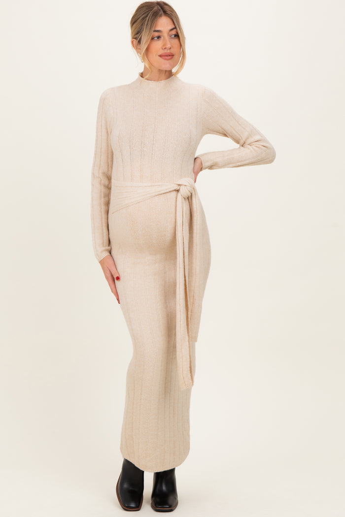 woman wearing a cream long sleeve knitted maternity dress with a tie belt and visible baby bump