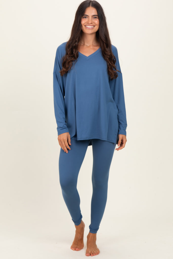 woman wearing a blue long sleeve v-neck top and matching leggings, standing barefoot against a neutral background