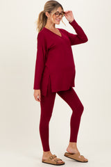 woman wearing a burgundy maternity top and leggings, showcasing her baby bump while posing with glasses