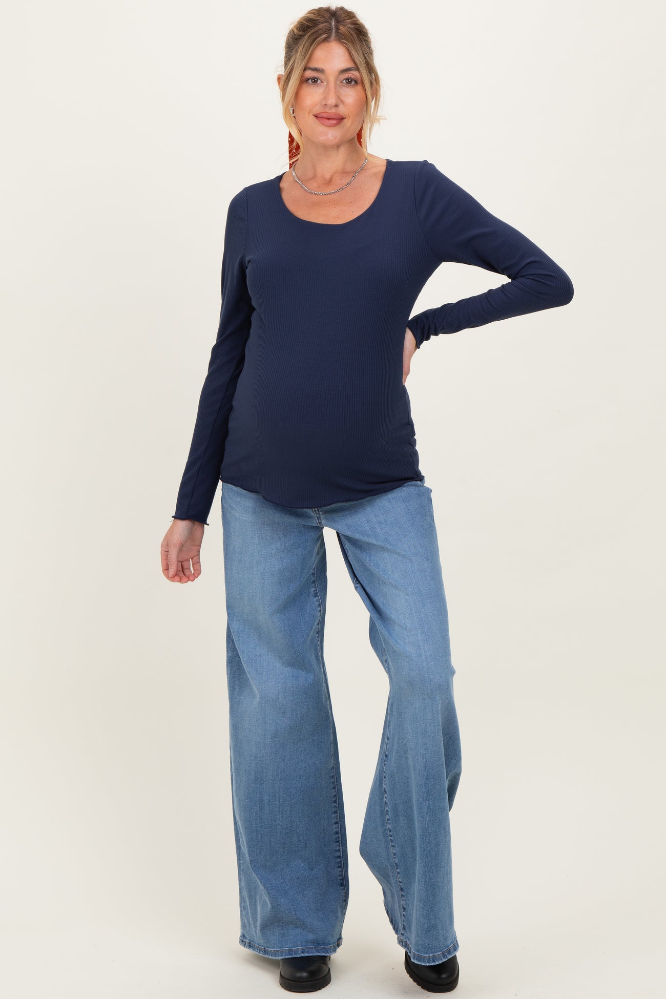 woman wearing a navy long sleeve maternity top and light blue wide-leg jeans, showing baby bump