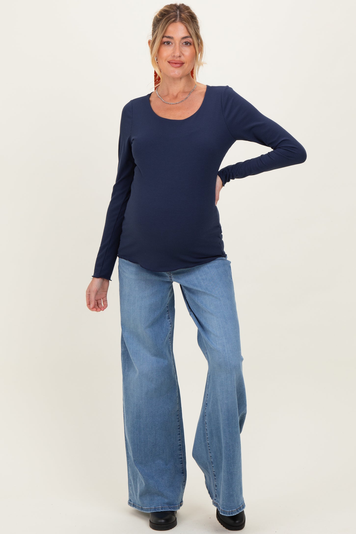 woman wearing a navy long sleeve maternity top and light blue wide-leg jeans, showing baby bump