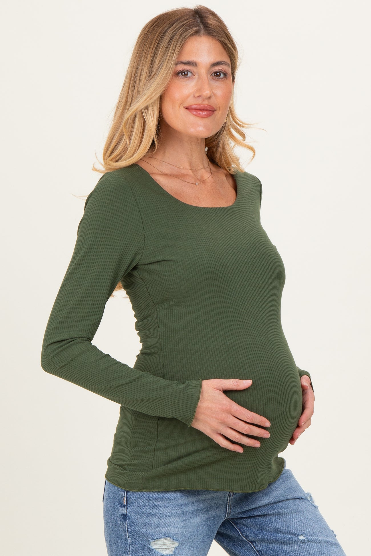 woman wearing an olive green long sleeve maternity top and holding her baby bump