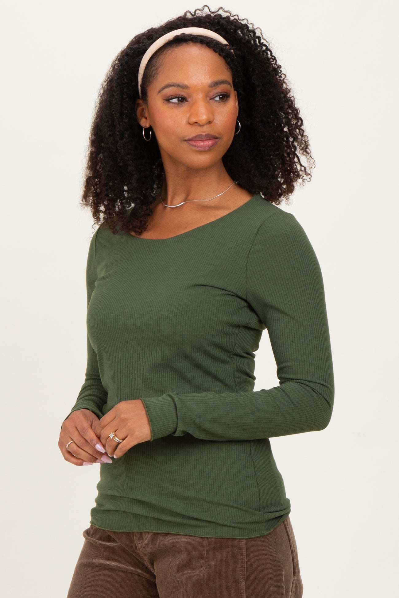 woman wearing a dark green ribbed long sleeve top, styled with a headband and silver jewelry