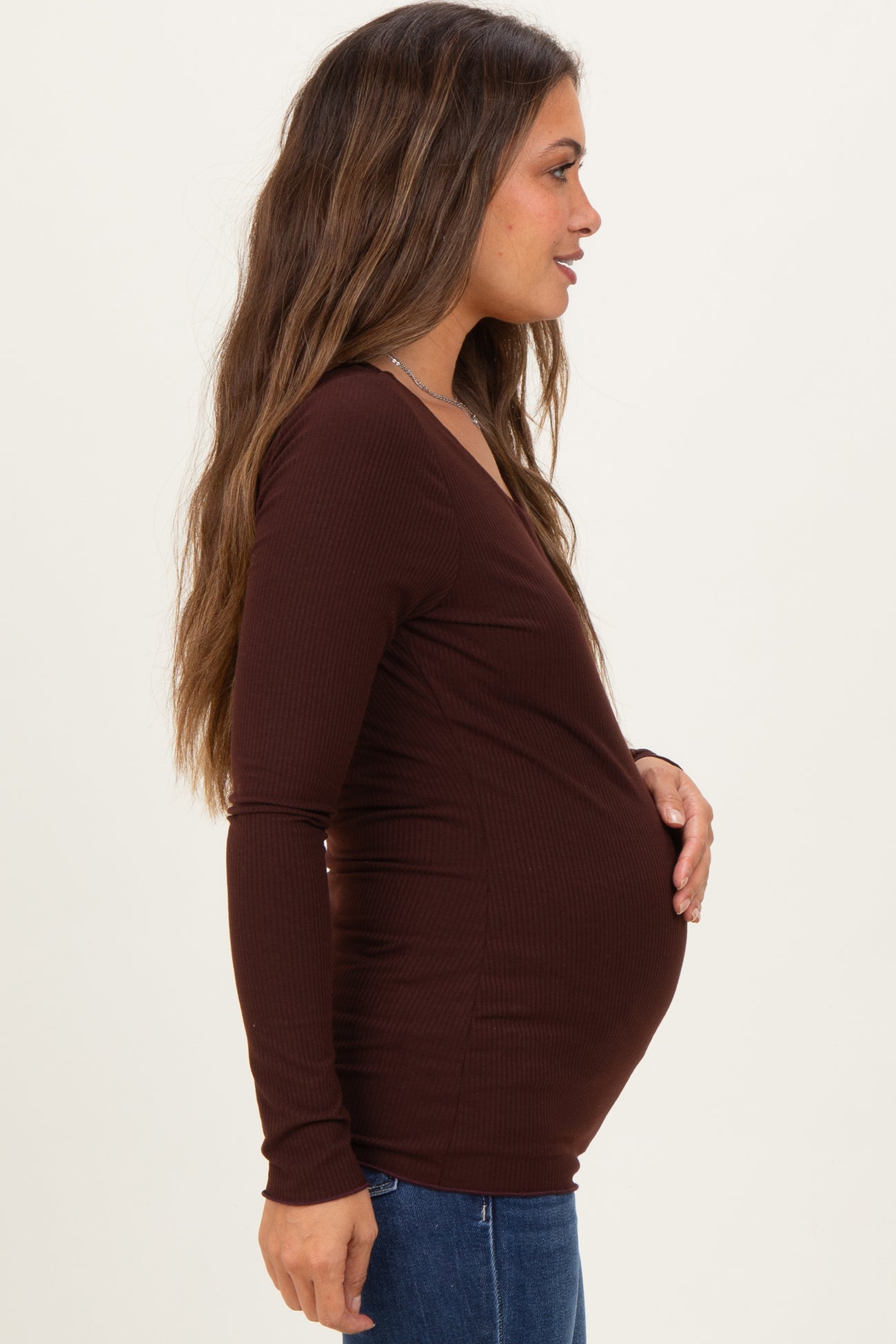woman wearing a dark brown long sleeve maternity top and holding her baby bump