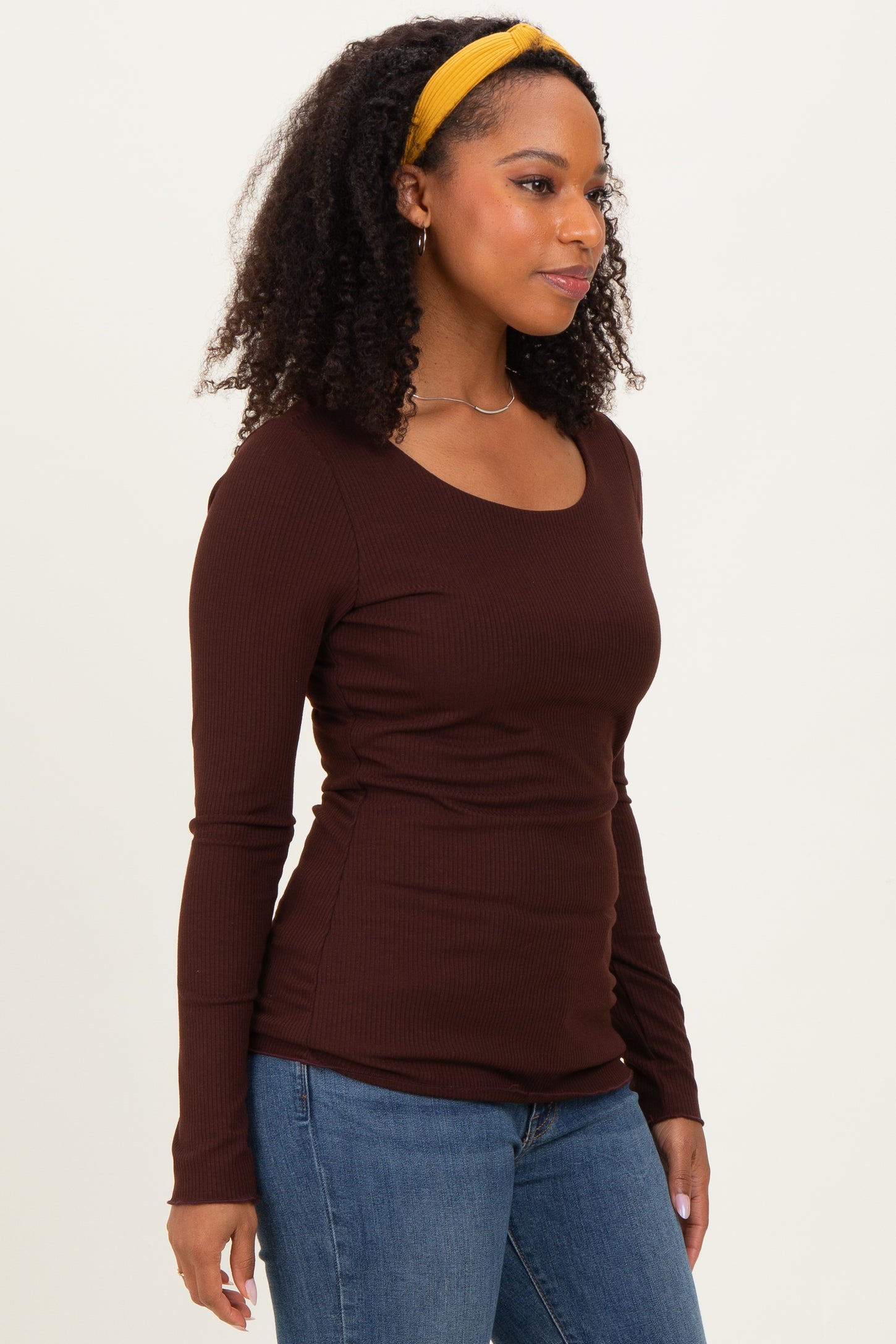 woman wearing a brown ribbed long sleeve top paired with blue jeans and a yellow headband