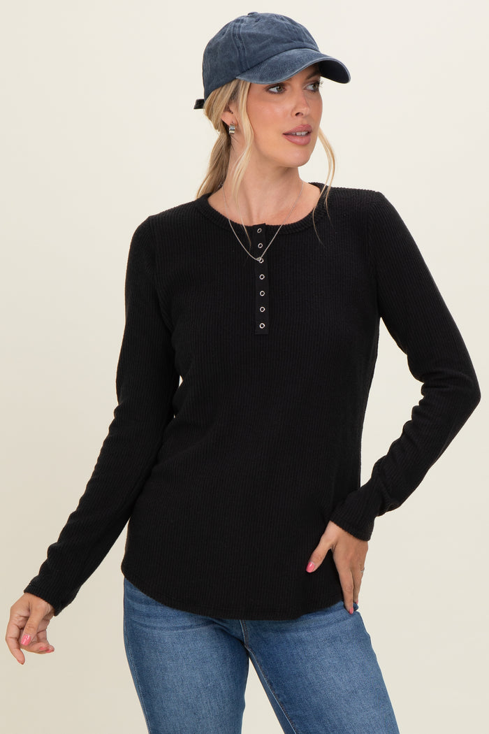 woman wearing a black long sleeve henley top with button details and a blue cap, paired with jeans