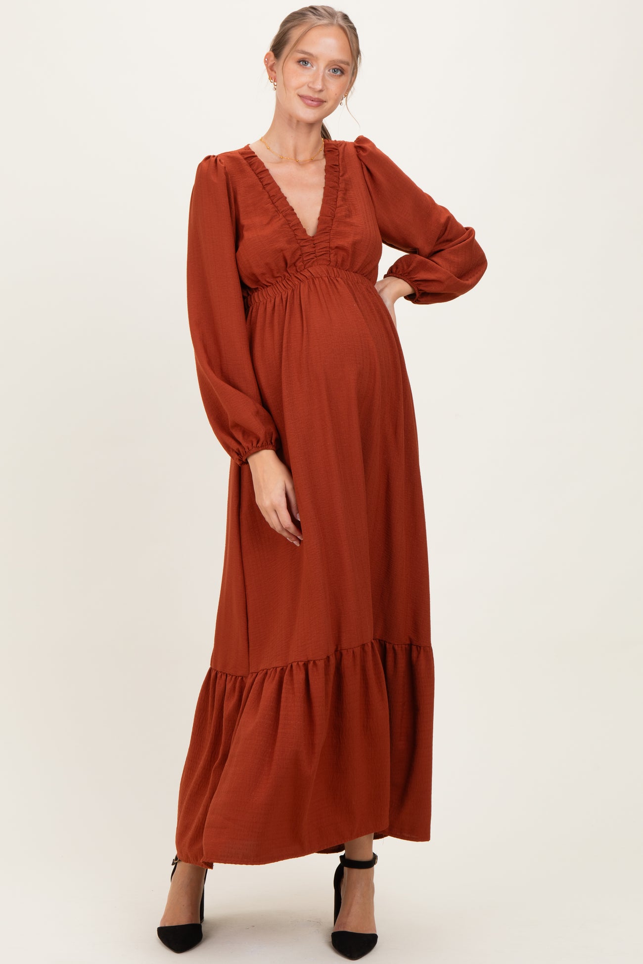 woman wearing a rust-colored long sleeve maternity maxi dress with ruffle details and a visible baby bump