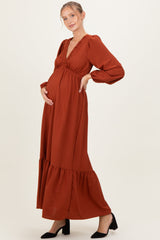 woman wearing a rust-colored maternity maxi dress with balloon sleeves and ruffle hem, showcasing her baby bump