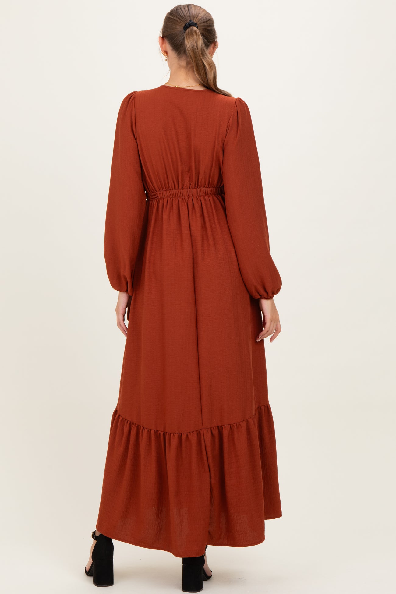 woman wearing a rust-colored long sleeve maternity maxi dress with an elastic waist and tiered hemline
