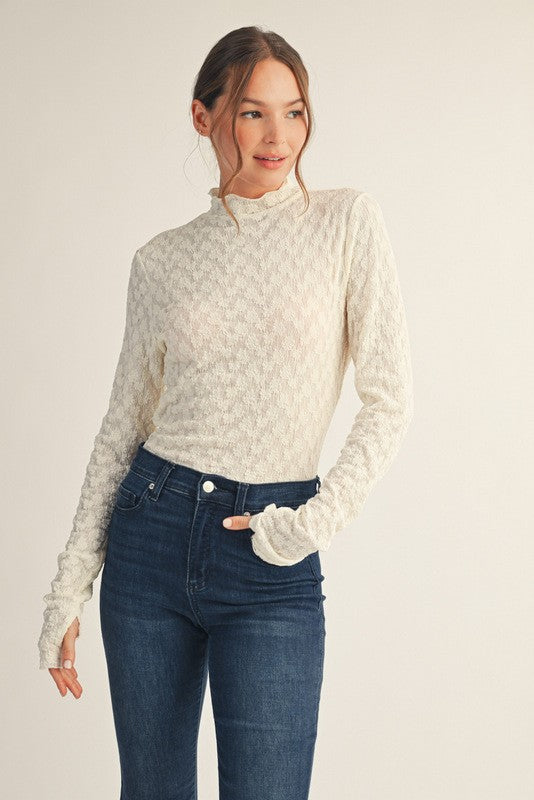 woman wearing a cream long sleeve textured top with a high neck and fingerless cuffs, paired with dark blue jeans