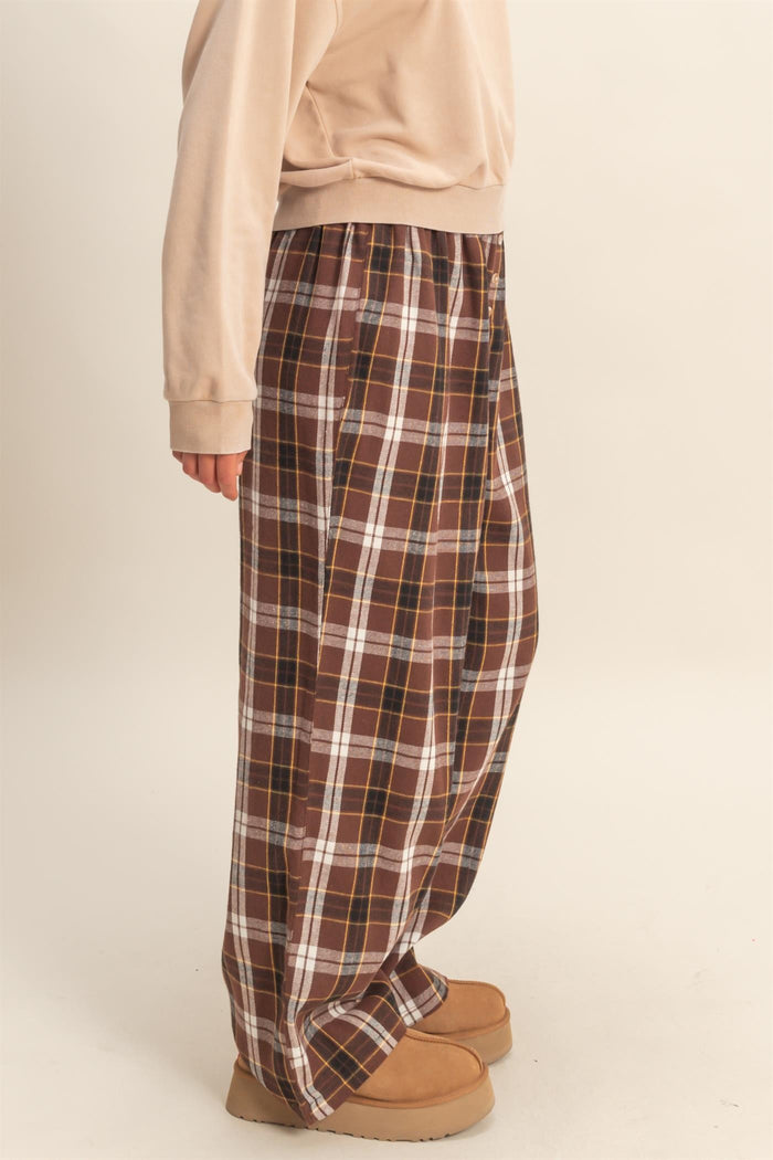 woman wearing brown plaid wide-leg pants, styled casually with a loose beige top and cozy footwear