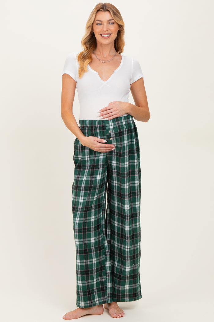 woman wearing a white short sleeve v-neck maternity top and green plaid maternity pants, holding her baby bump