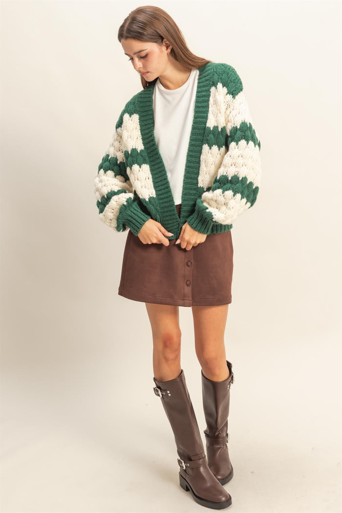 woman wearing a green and cream chunky knit cardigan with puff sleeves, styled with a brown suede mini skirt and knee-high boots