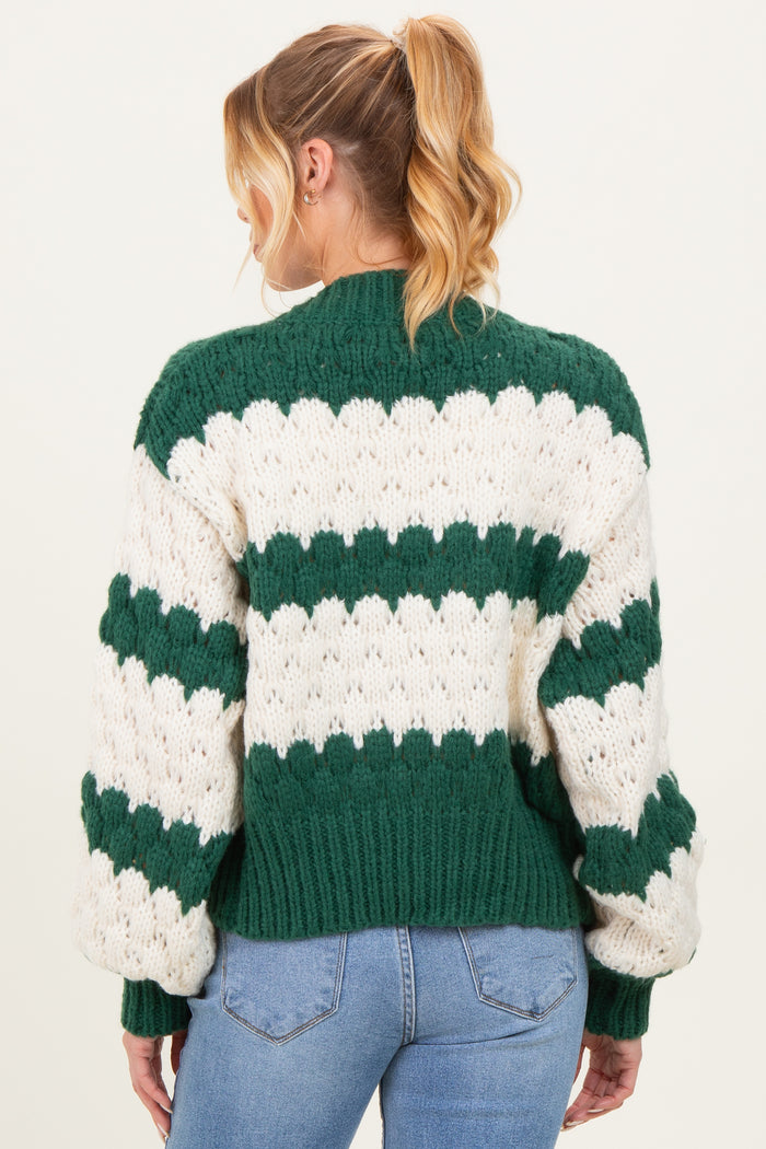 woman wearing a green and white striped chunky knit maternity sweater, showing the back and oversized sleeves