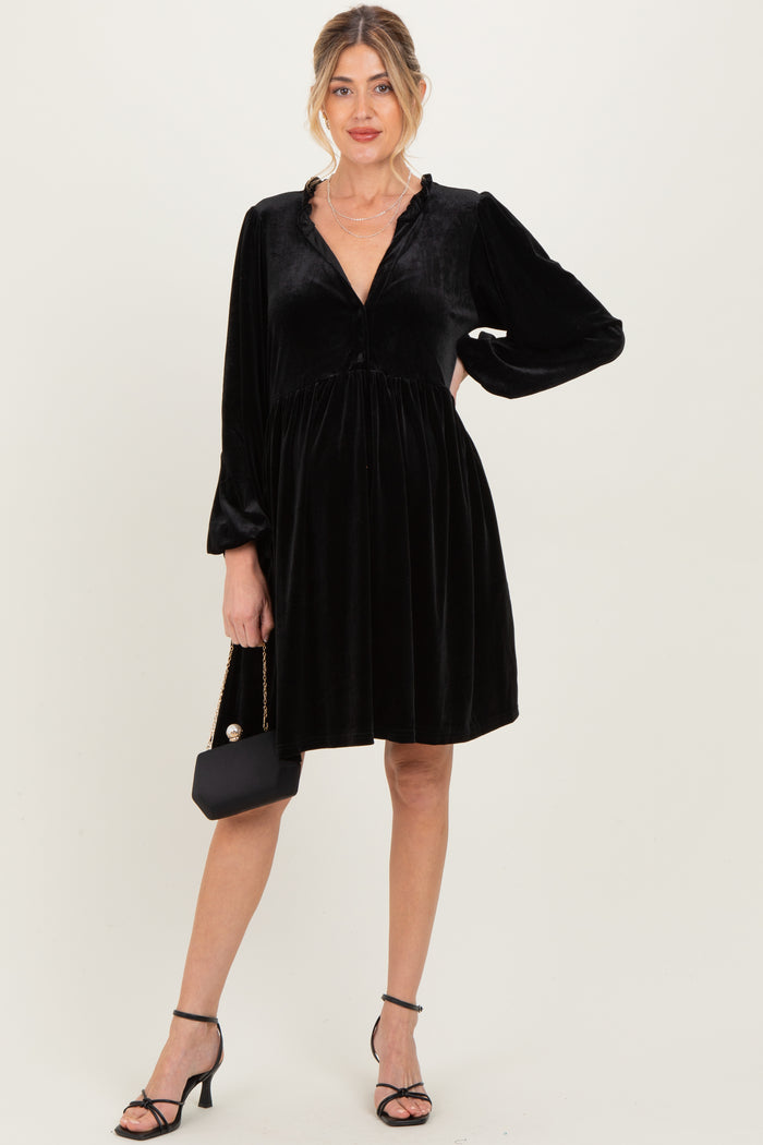 woman wearing a black velvet maternity dress with long sleeves and a flowing skirt, holding a small black purse