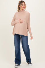 woman wearing a light pink long sleeve maternity top and blue wide-leg jeans, holding her baby bump