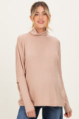 woman wearing a light brown maternity turtleneck top with a relaxed fit and a baby bump visible