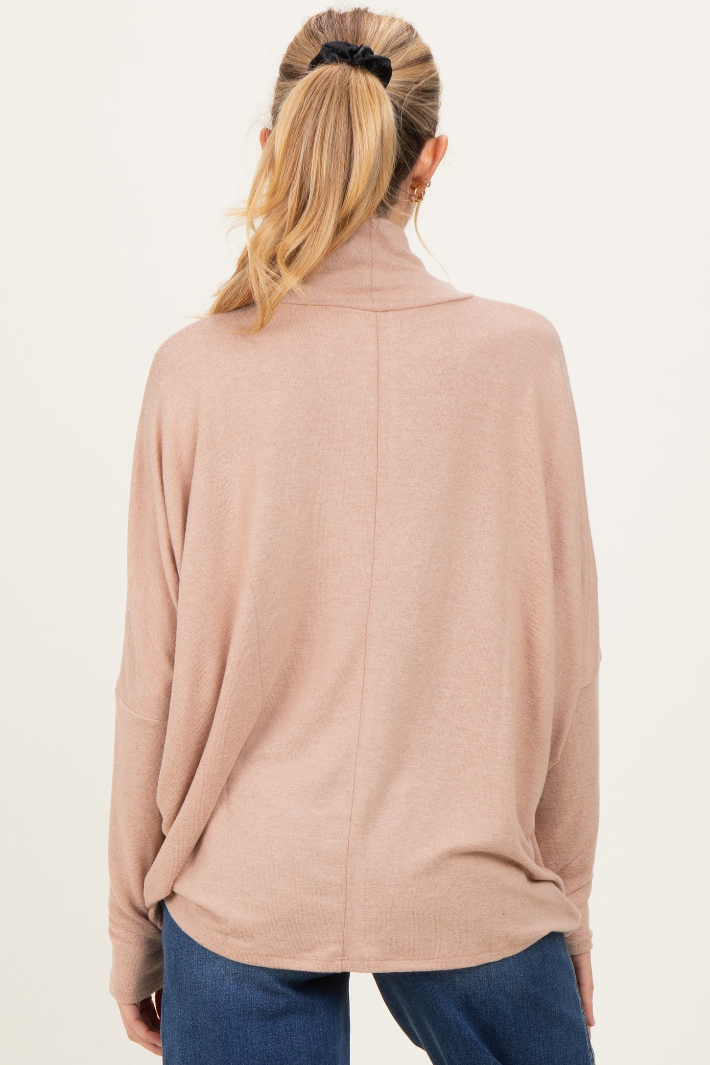woman wearing a light pink oversized maternity sweater with a high collar, viewed from the back