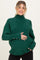 woman wearing a dark green maternity turtleneck sweater with button details and holding her baby bump