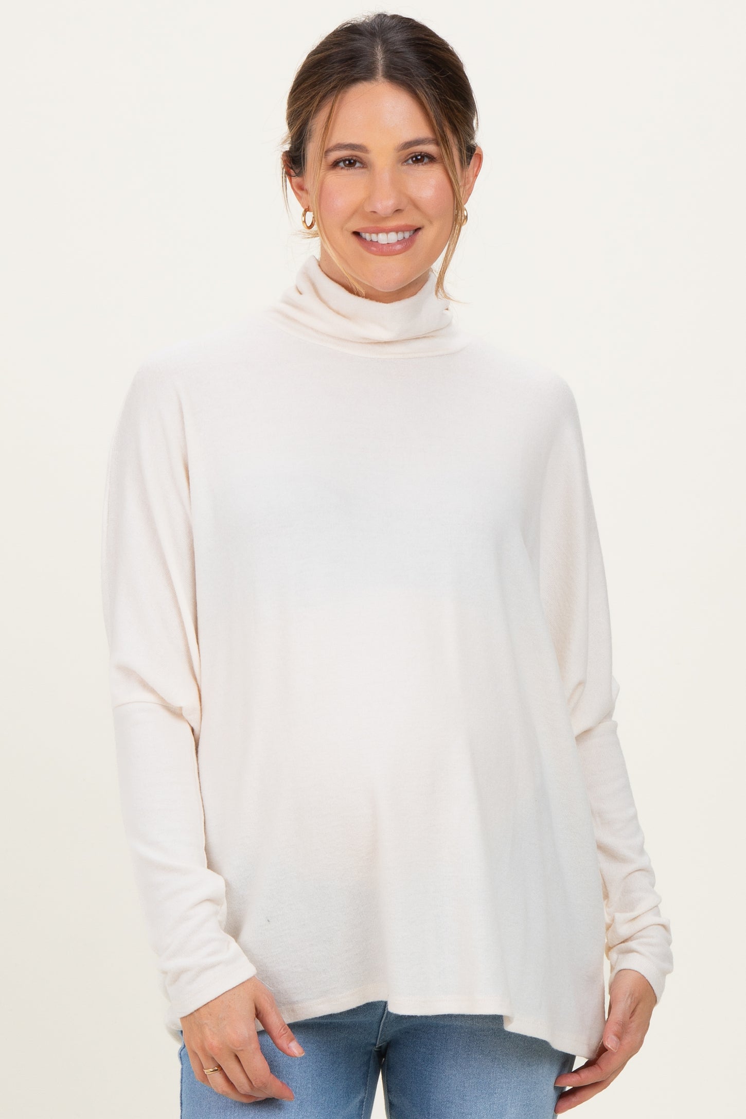 woman wearing a beige maternity turtleneck sweater and blue jeans, showing her baby bump