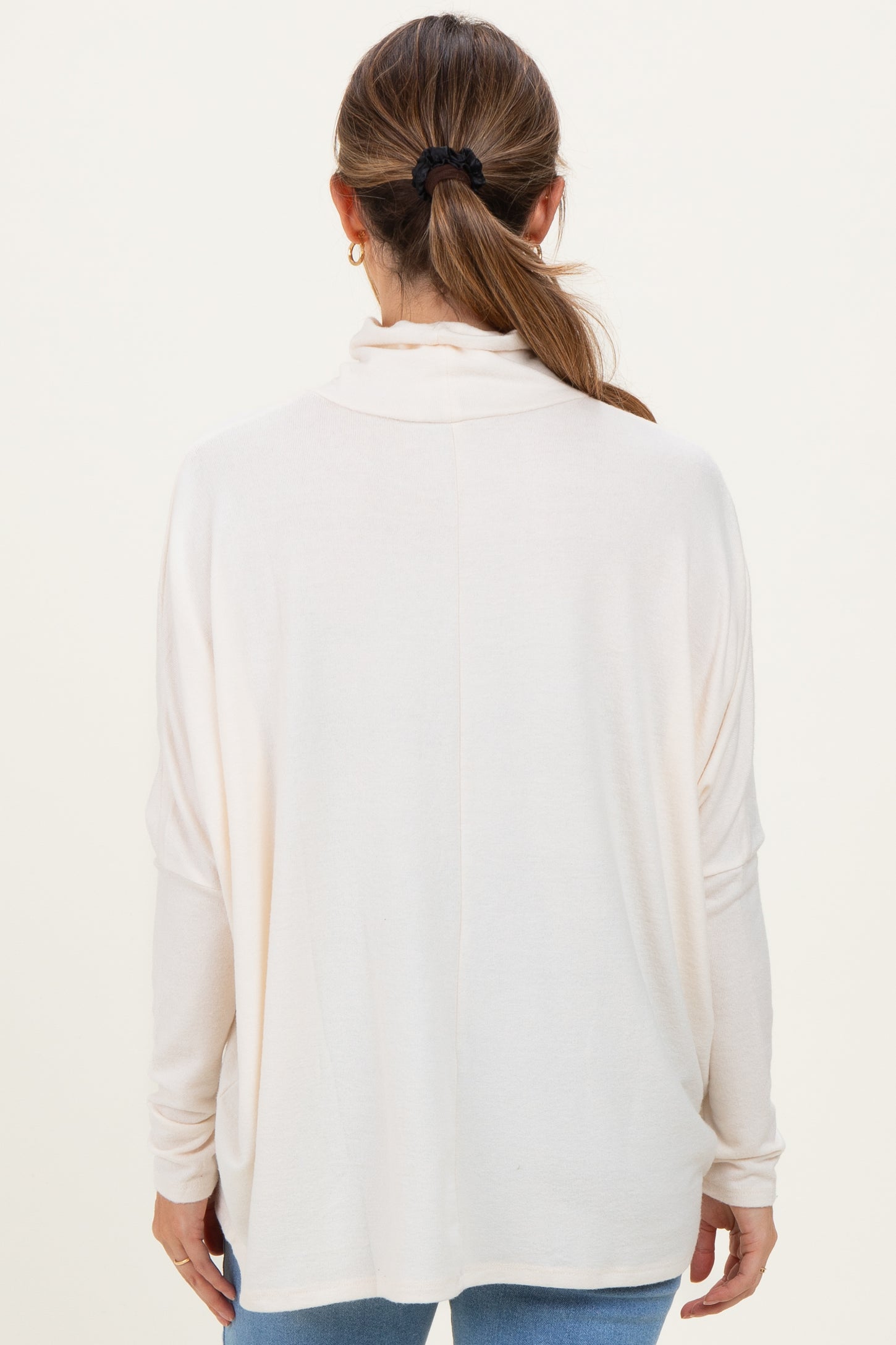 woman wearing a cream long sleeve maternity top, viewed from the back, with relaxed fit and draped neckline
