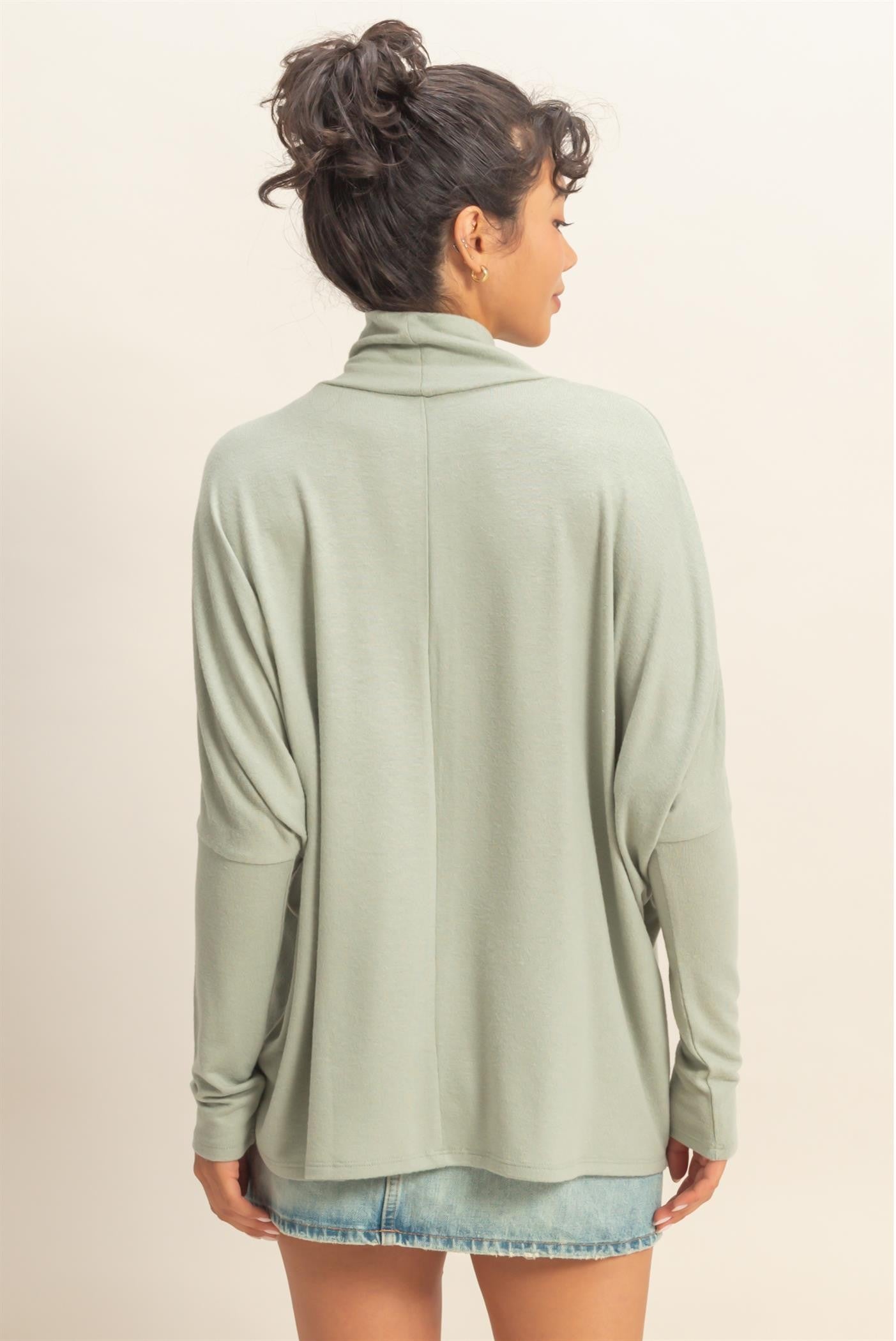 woman wearing a light green long sleeve pullover with a relaxed fit and back drape detail, styled with a denim mini skirt