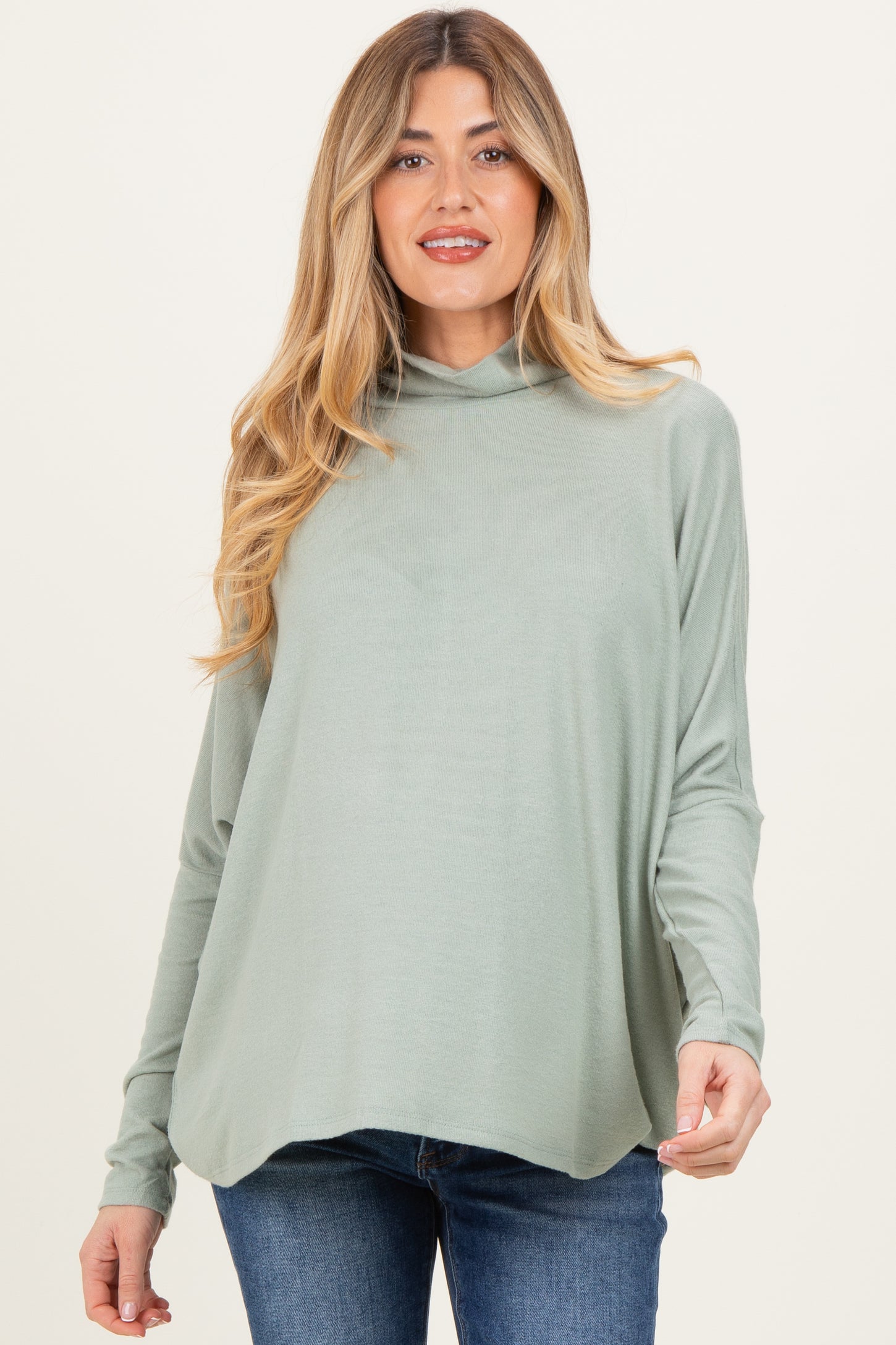 woman wearing a light green maternity top with a cowl neckline and long sleeves, paired with dark denim jeans