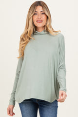 woman wearing a light green maternity top with a cowl neckline and long sleeves, paired with dark denim jeans