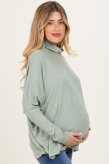woman wearing a soft green long sleeve maternity top with a cowl neck and holding her baby bump