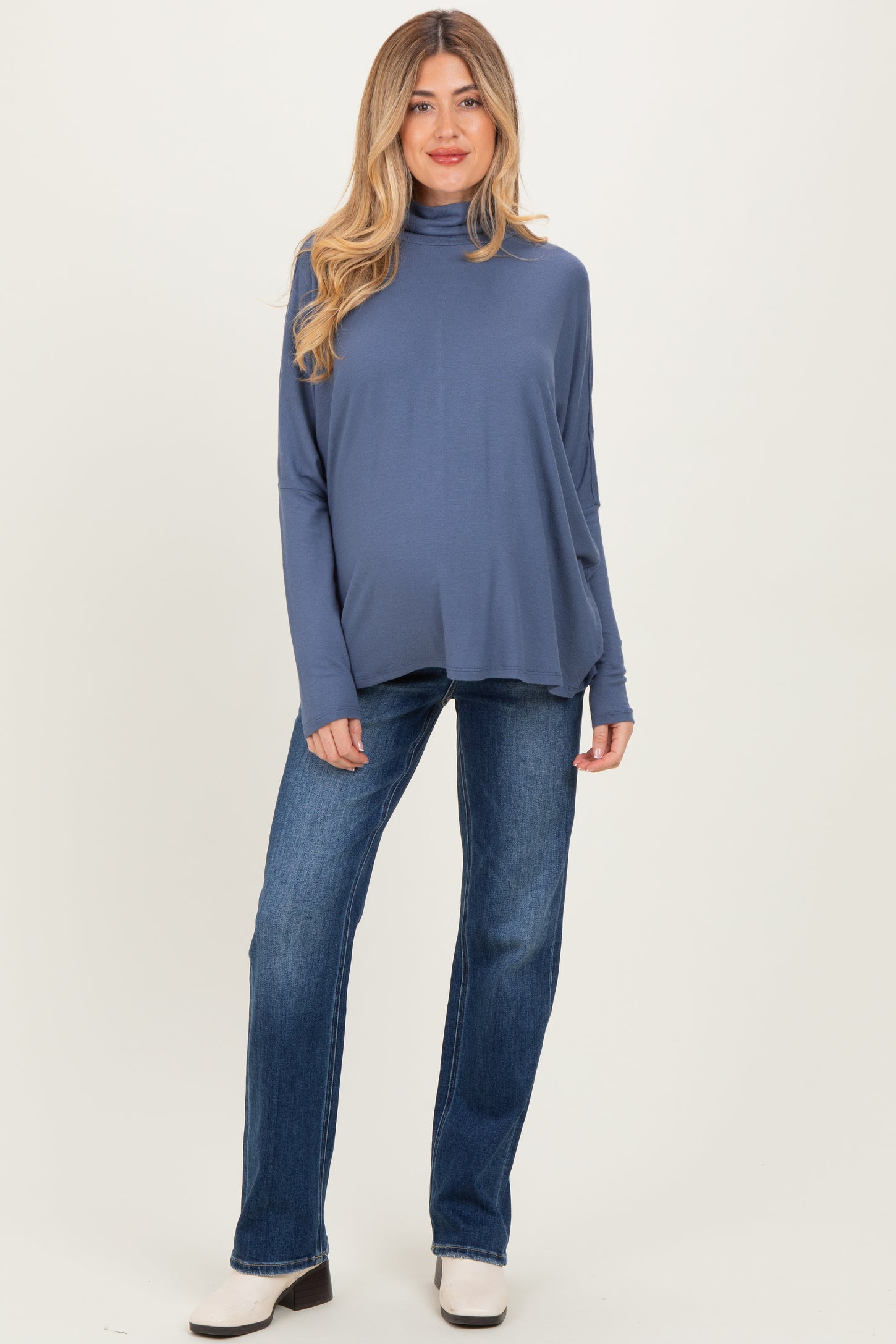 woman wearing a dusty blue maternity turtleneck top and blue jeans, showcasing her baby bump