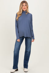 woman wearing a dusty blue maternity turtleneck top and blue jeans, showcasing her baby bump