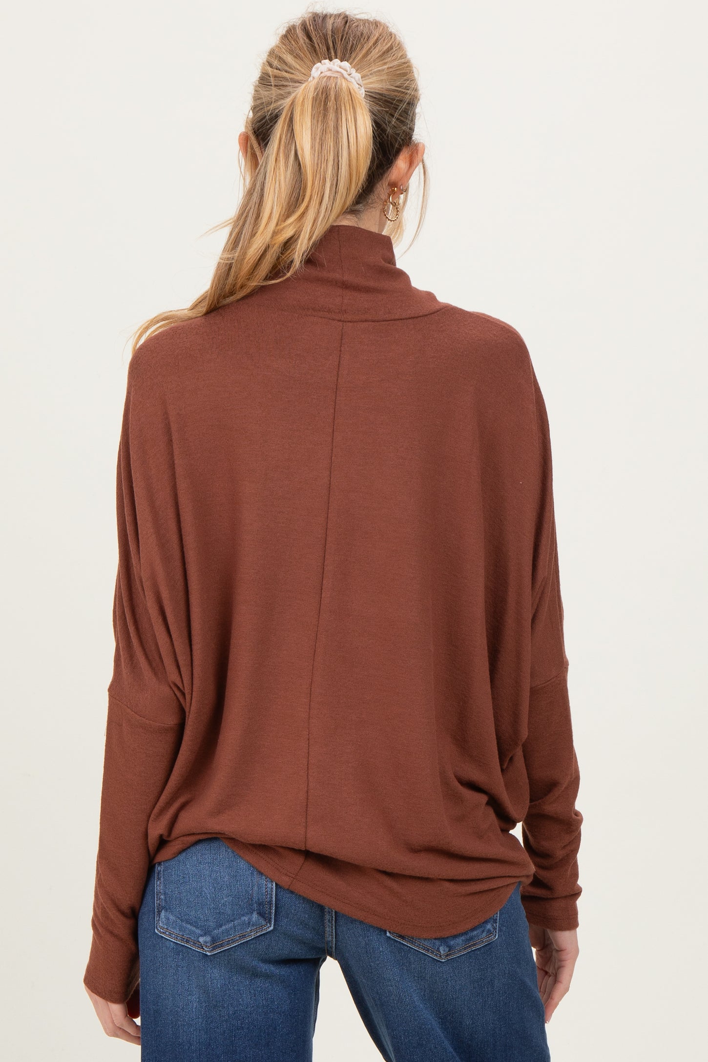 woman wearing a rust-colored maternity sweater with a relaxed fit and high collar, viewed from the back