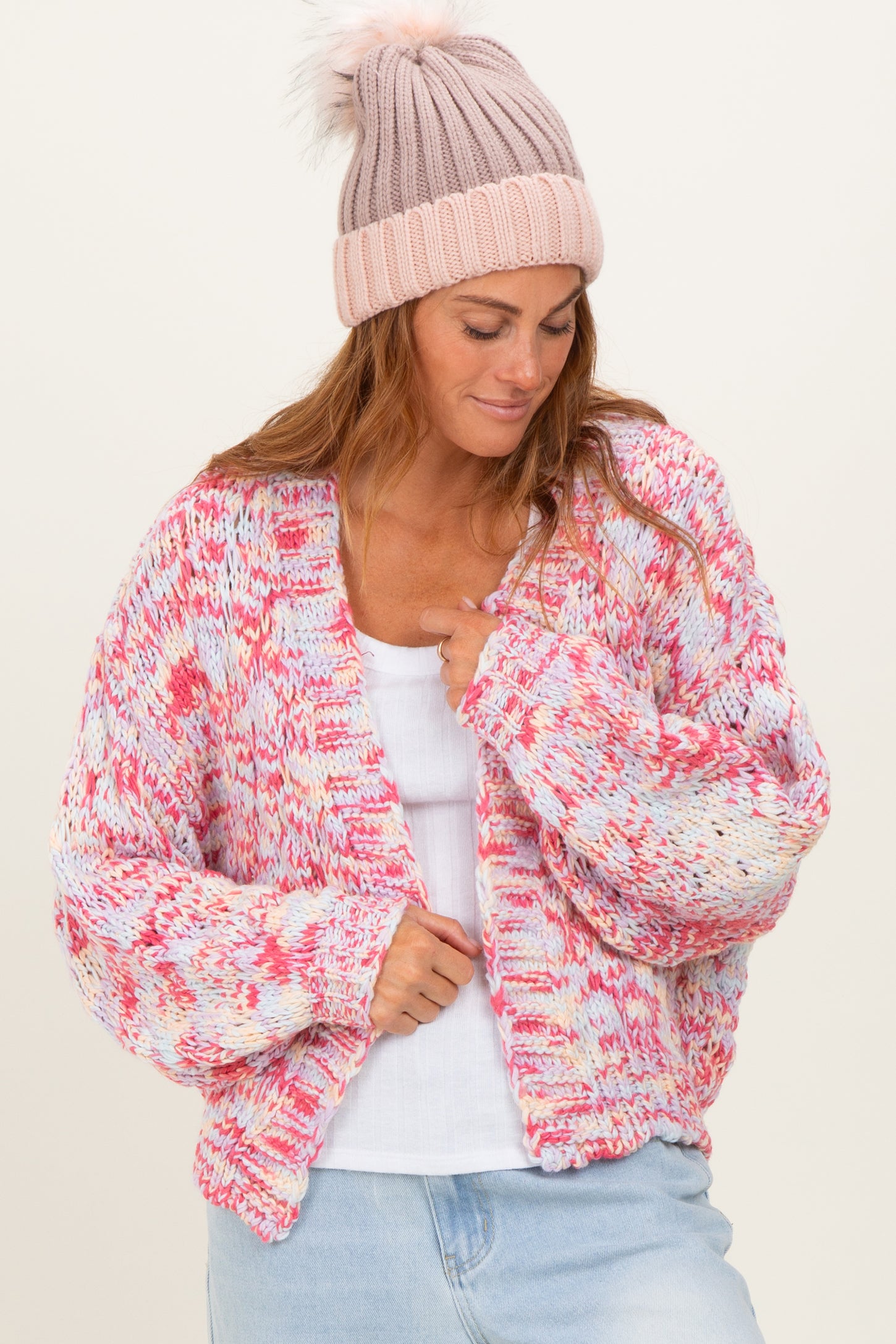 woman wearing a colorful oversized knitted cardigan and a pink beanie, styled with a white tank top and light blue jeans