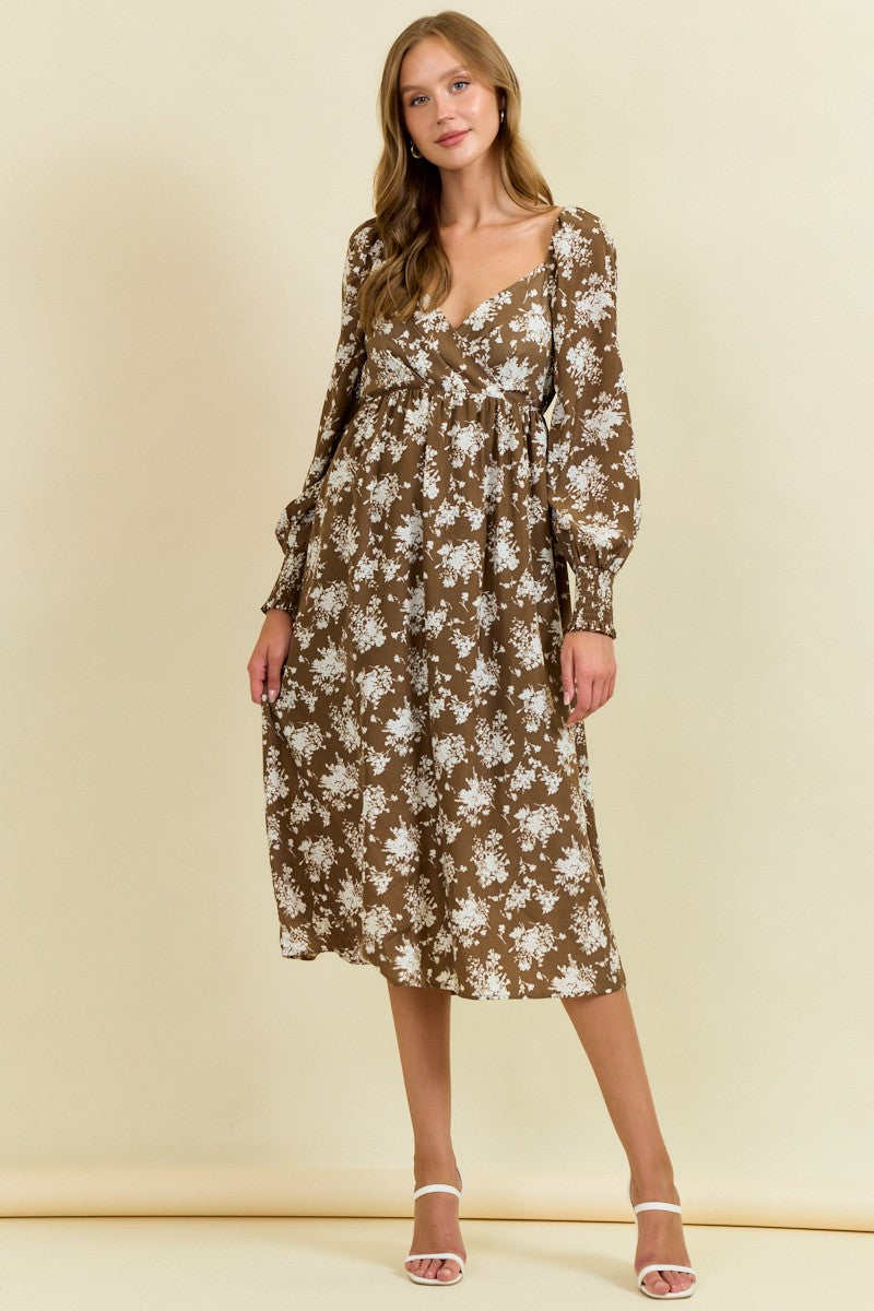 woman wearing a brown floral midi dress with long sleeves and a loose fit, standing against a beige background