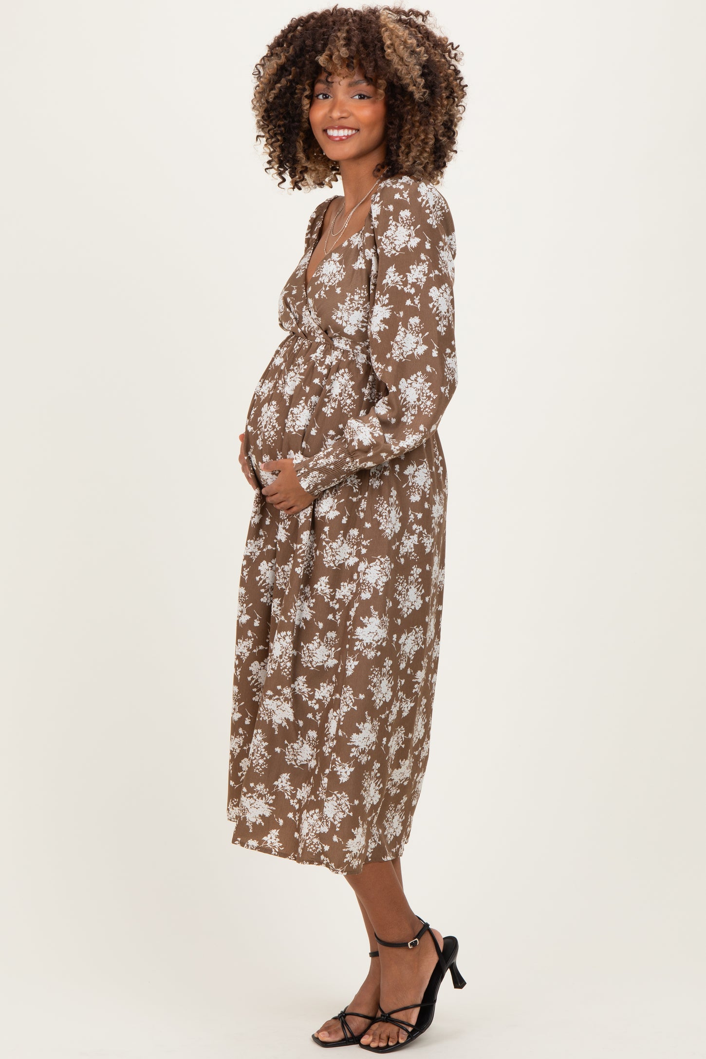 woman wearing a brown floral maternity dress and cradling her baby bump