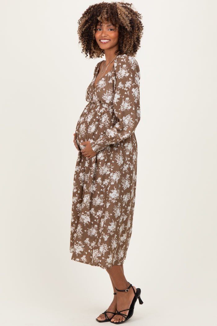 woman wearing a brown floral maternity dress and cradling her baby bump