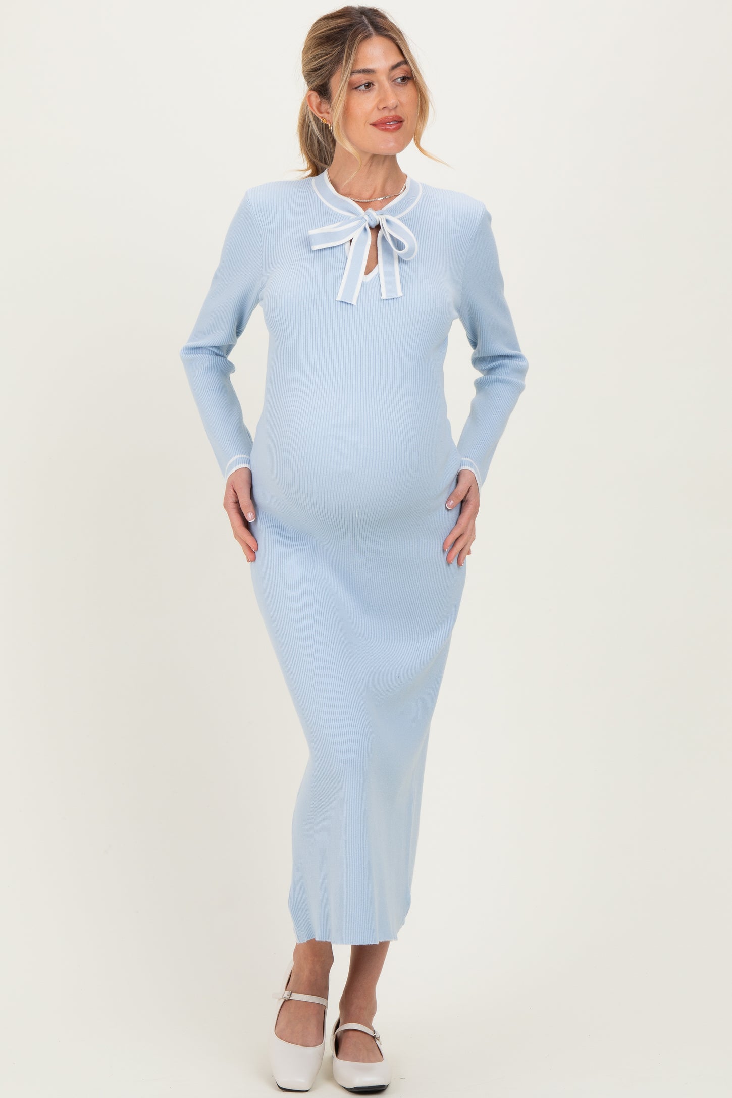 woman wearing a light blue ribbed maternity dress with long sleeves and a bow tie detail, showing her baby bump