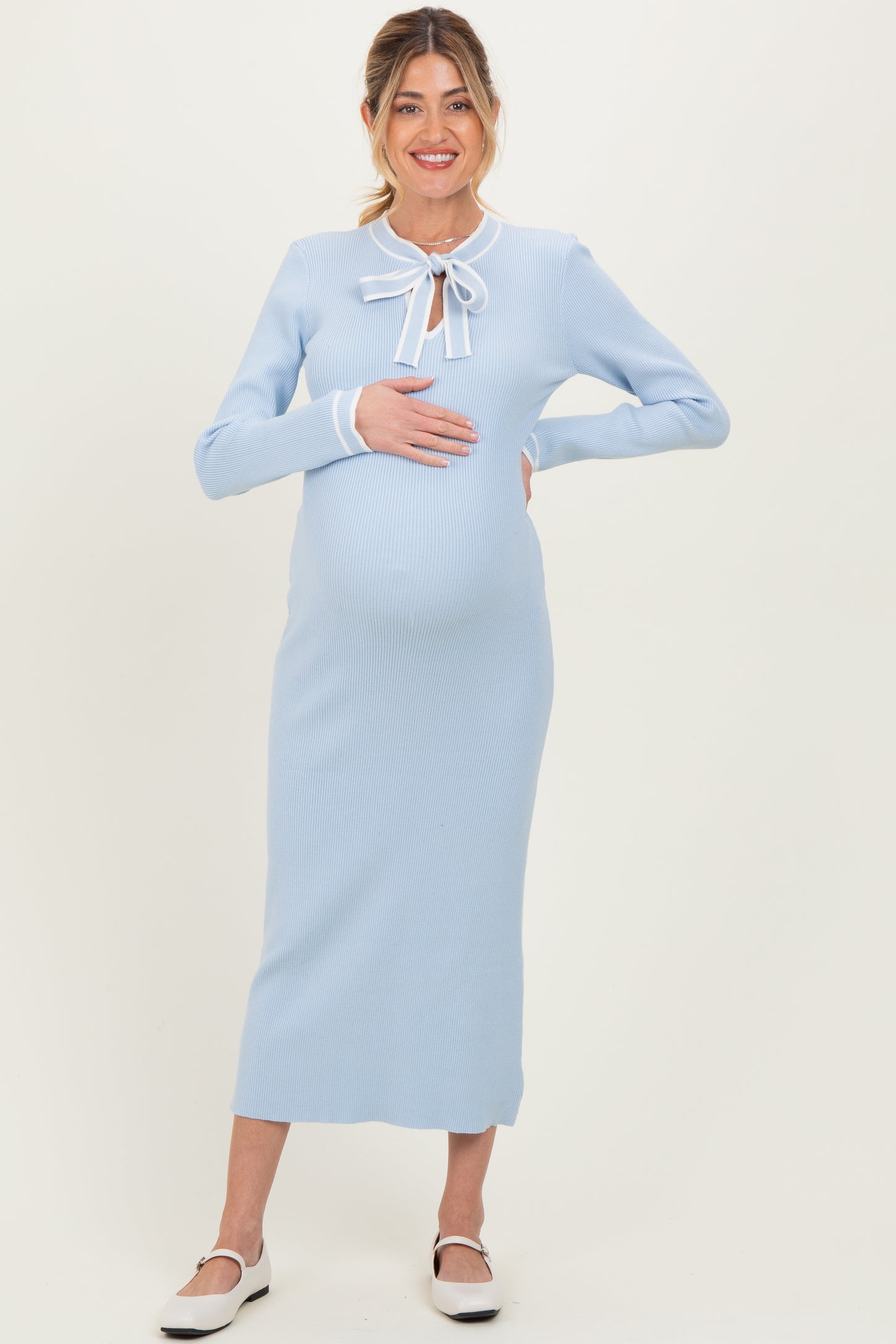 woman wearing a light blue ribbed maternity dress with a tie bow detail and holding her baby bump