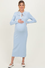 woman wearing a light blue ribbed maternity dress with a tie bow detail and holding her baby bump