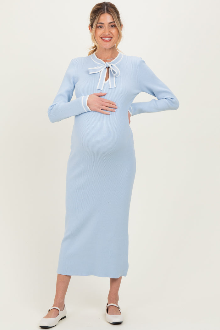woman wearing a light blue ribbed maternity dress with a tie bow detail and holding her baby bump