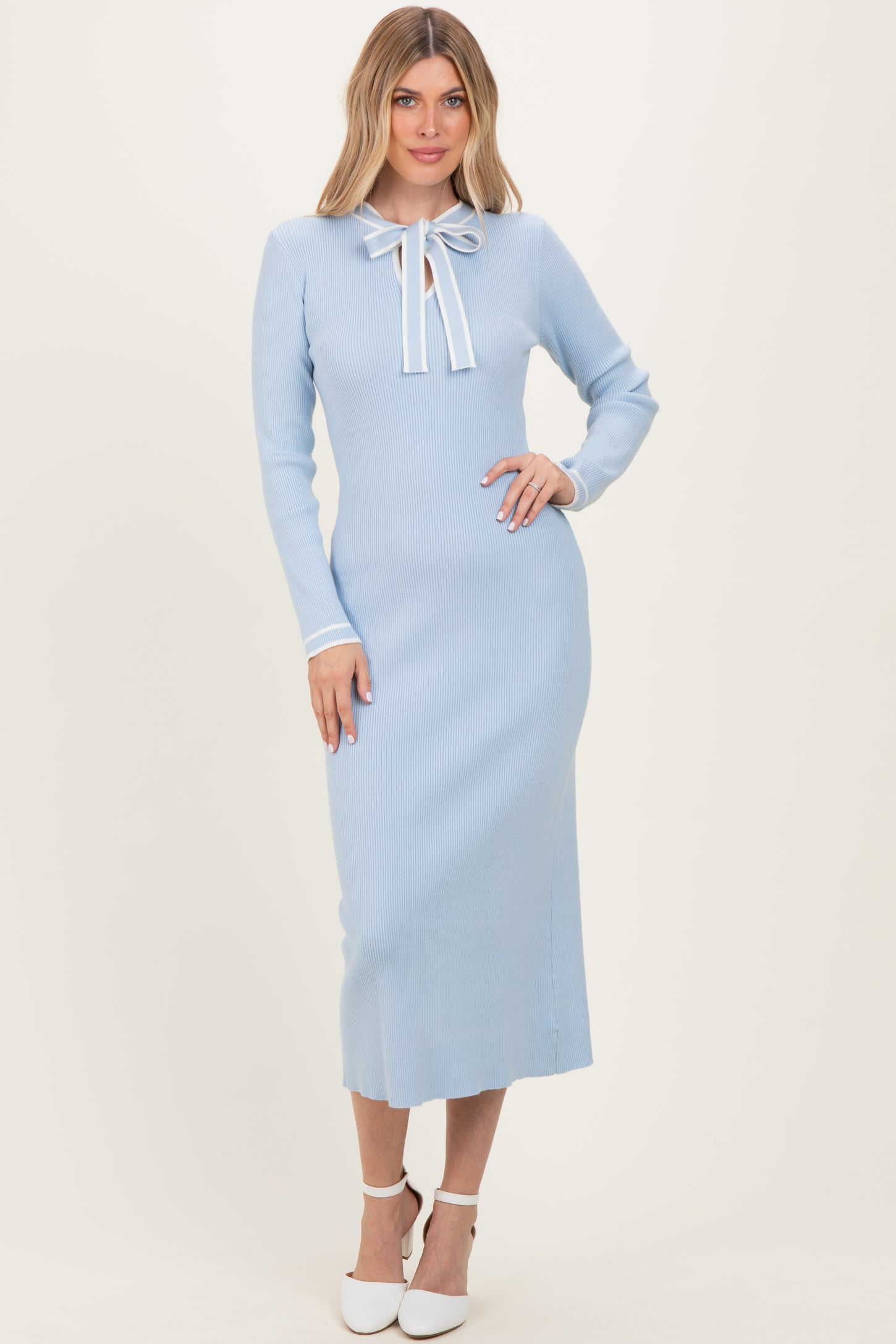 woman wearing a baby blue ribbed midi dress with long sleeves and a bow tie neck detail