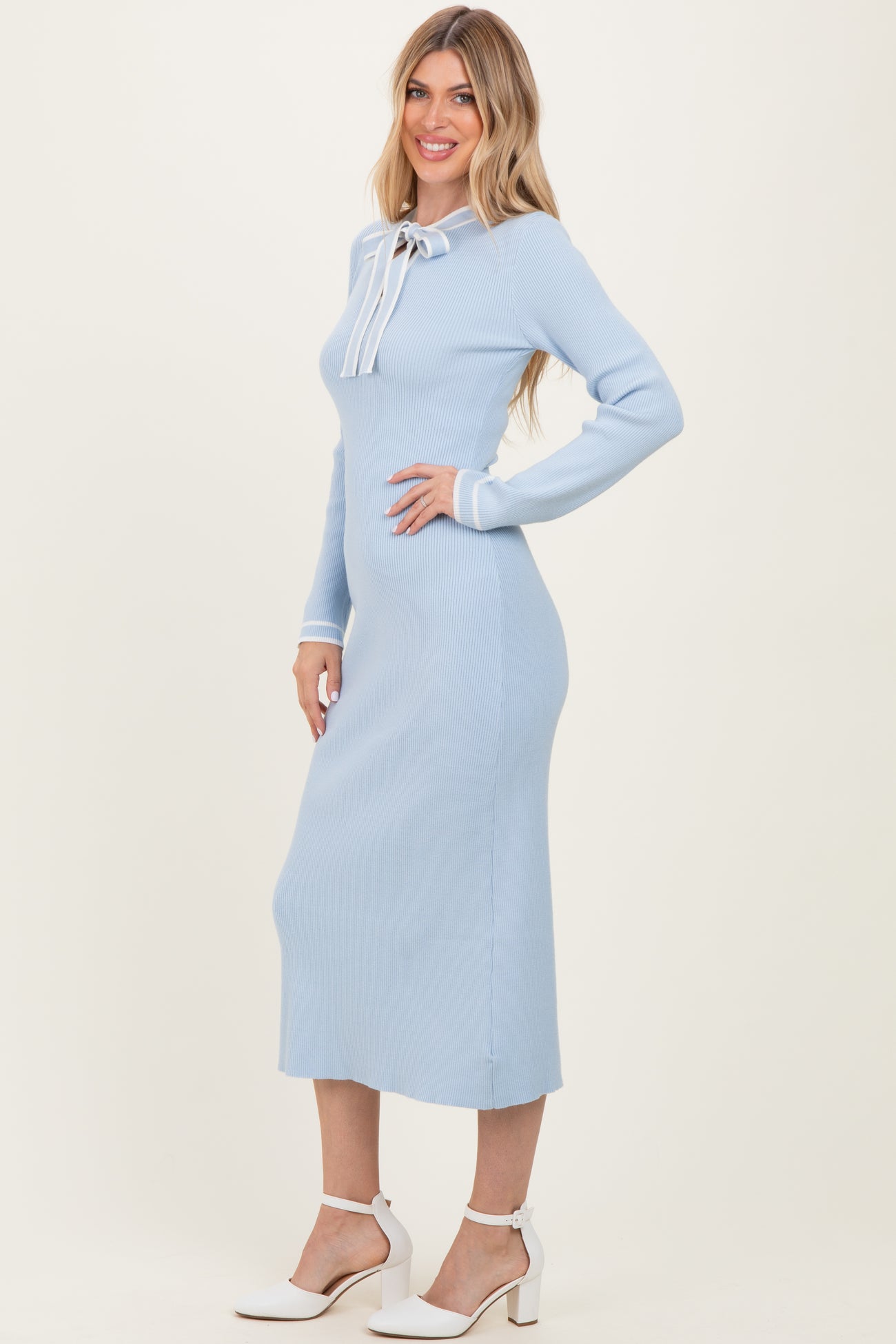 woman wearing a light blue ribbed midi dress with a bow tie detail at the neckline and long sleeves