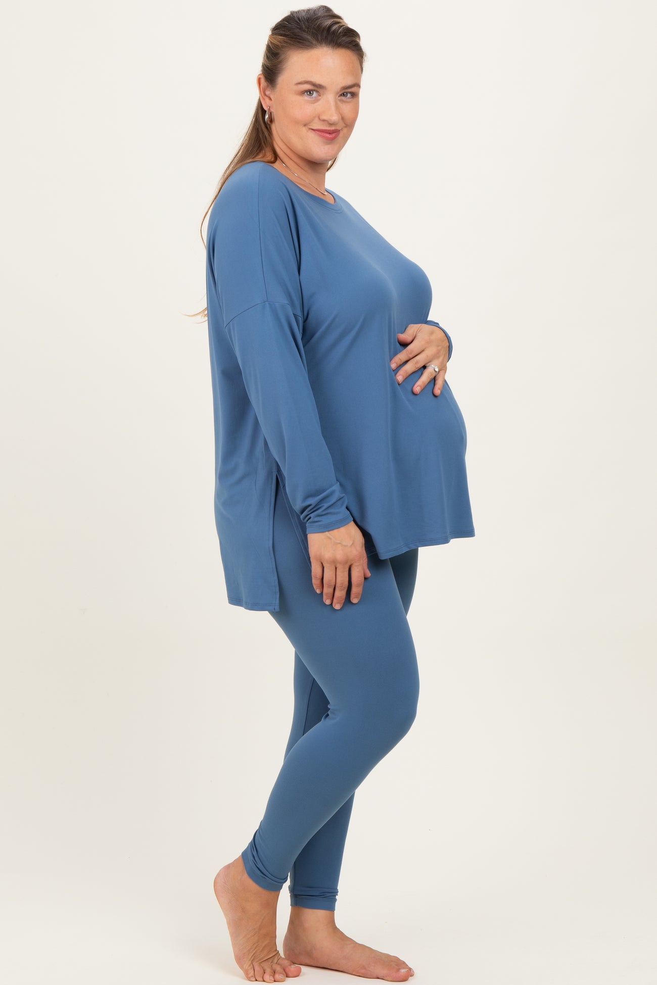 woman wearing a blue maternity plus long sleeve top and matching leggings, showcasing her baby bump