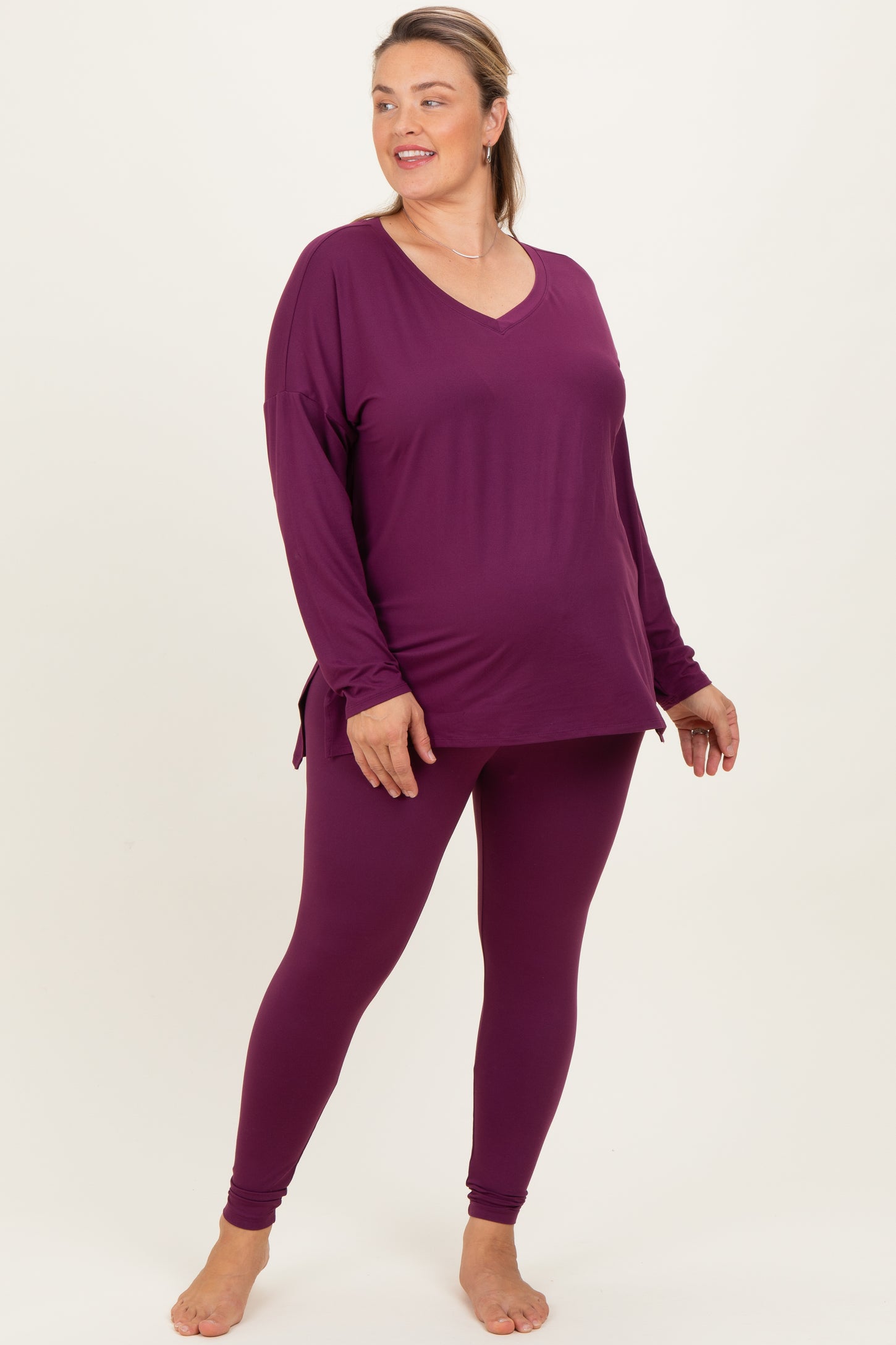 woman wearing a purple long sleeve maternity top and matching leggings, showing off her baby bump