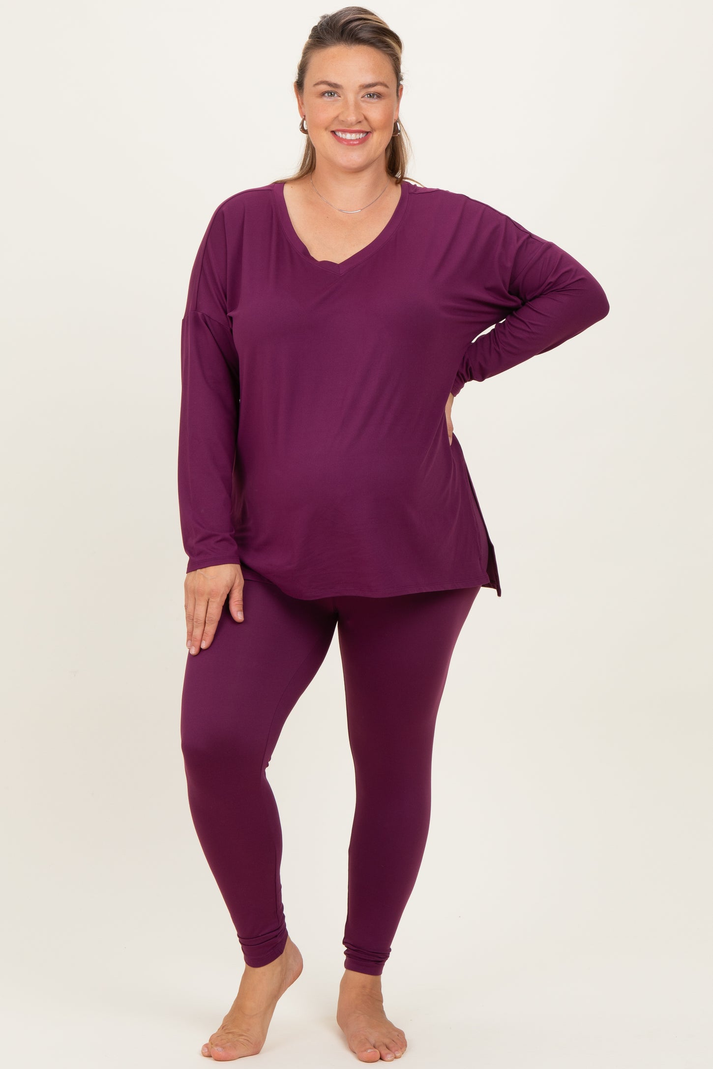 woman wearing a deep purple long sleeve maternity top and matching leggings, displaying her baby bump