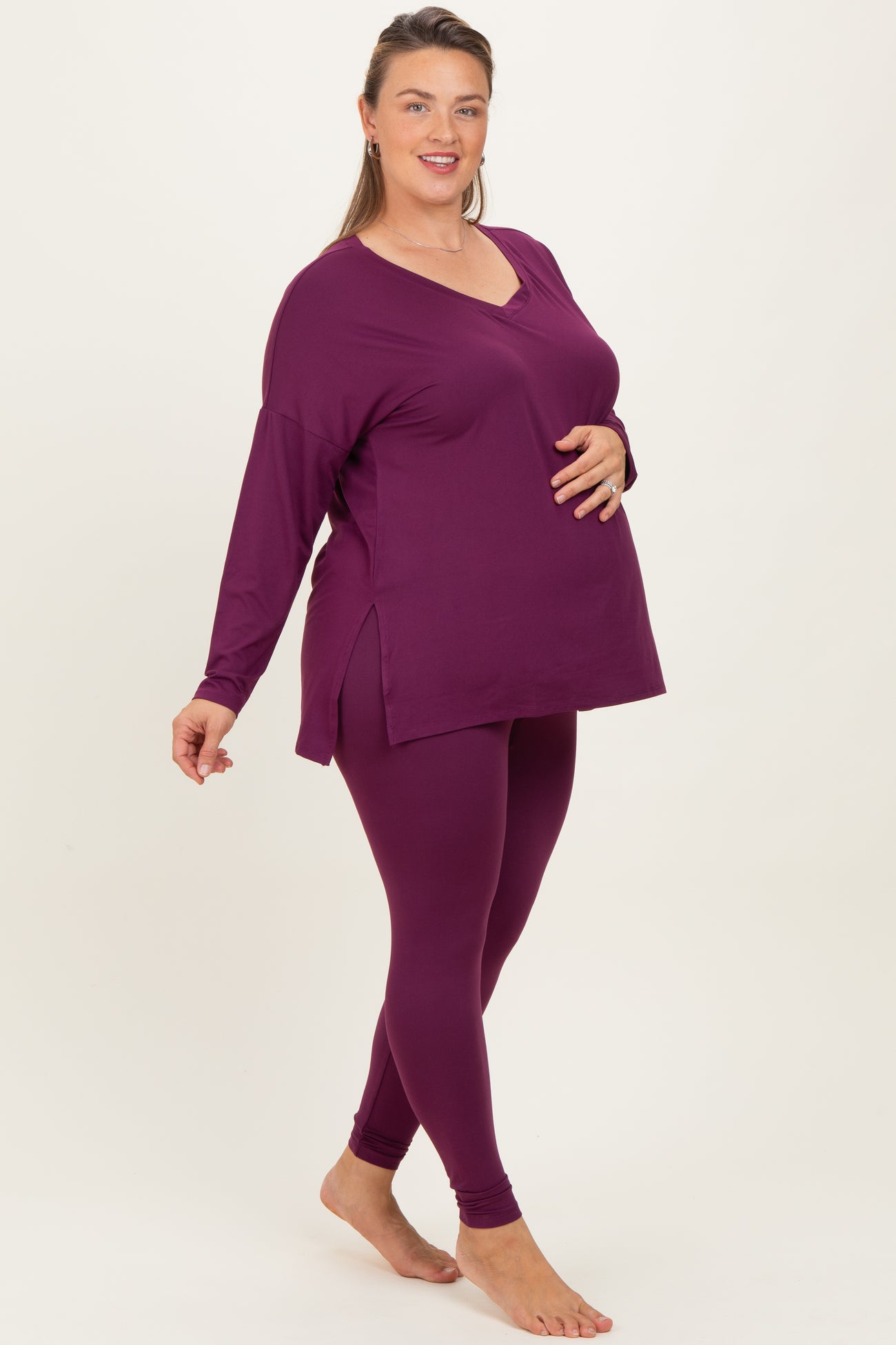 woman wearing a dark purple maternity plus long sleeve top and matching leggings, showing her baby bump