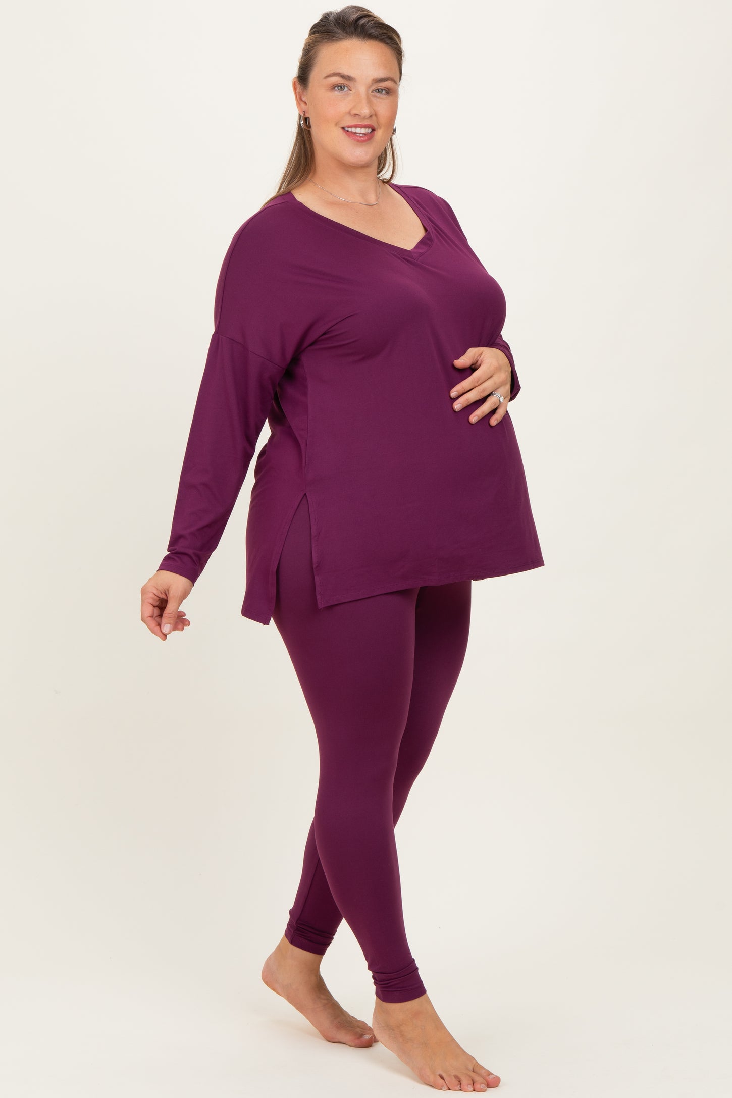 woman wearing a dark purple maternity plus long sleeve top and matching leggings, showing her baby bump