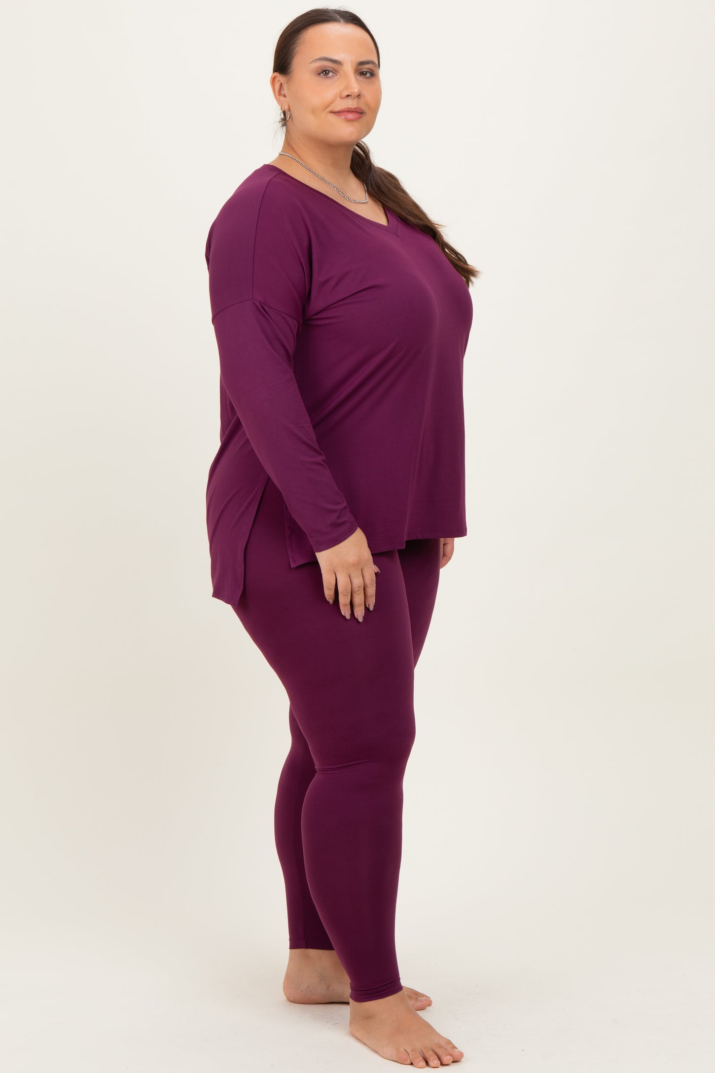woman wearing a burgundy long sleeve top and matching leggings in plus size, standing against a plain background