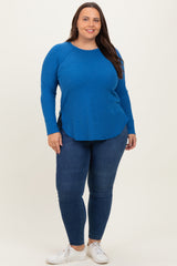 woman wearing a bright blue long sleeve top and dark blue skinny jeans, standing against a neutral background