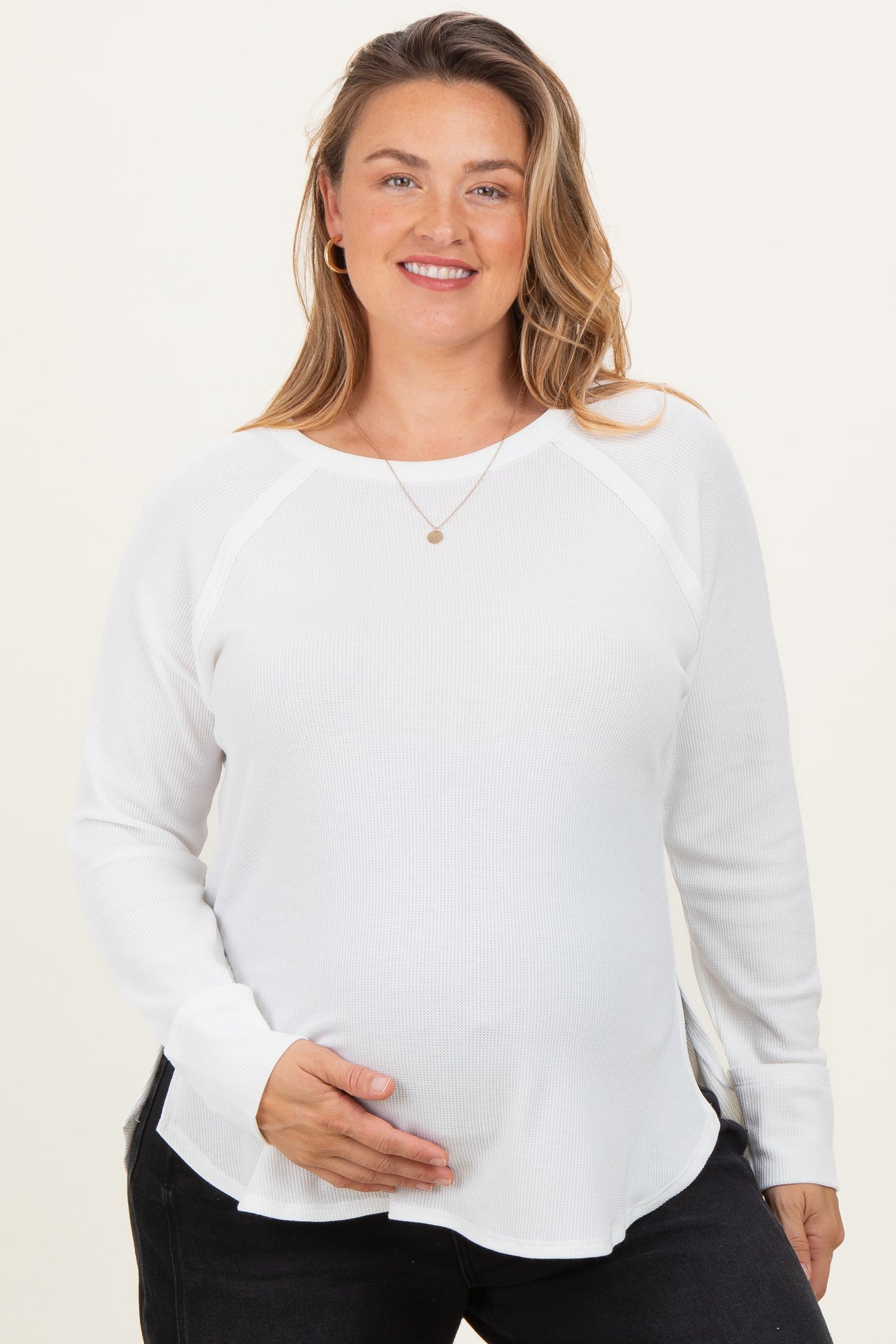 woman wearing a white long sleeve maternity top and holding her baby bump